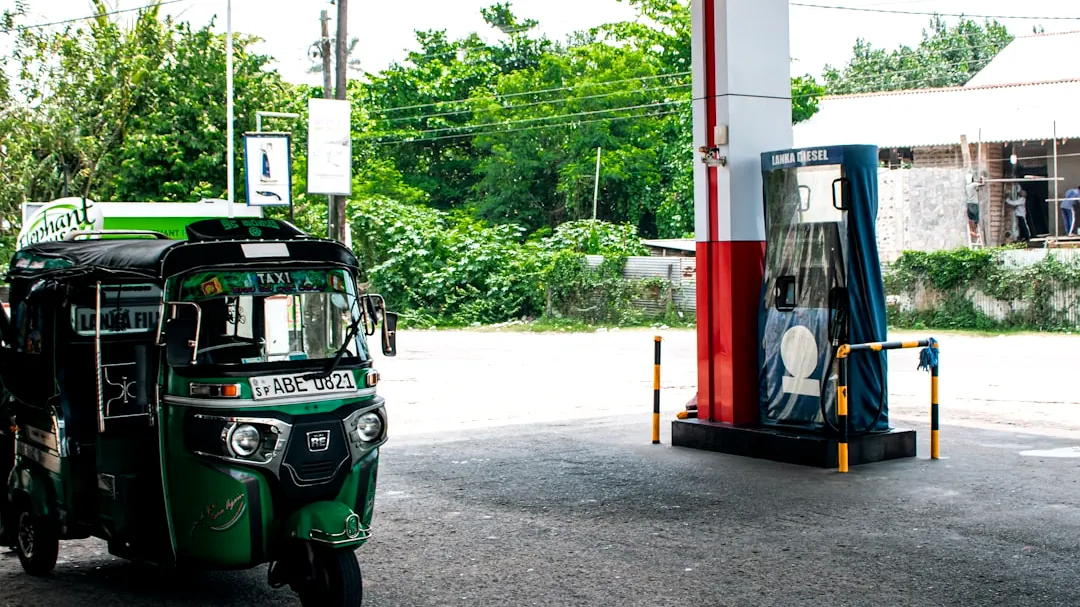 A green tuk-tuk at a gas station.