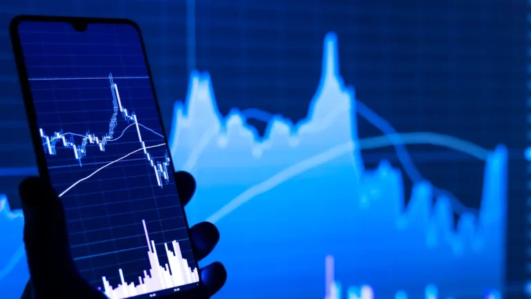 a person holding a cell phone in front of a stock chart