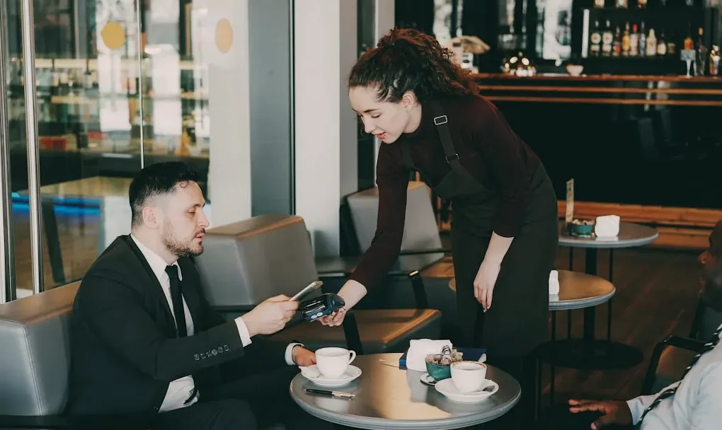 A woman serves coffee to a man in a cafe.