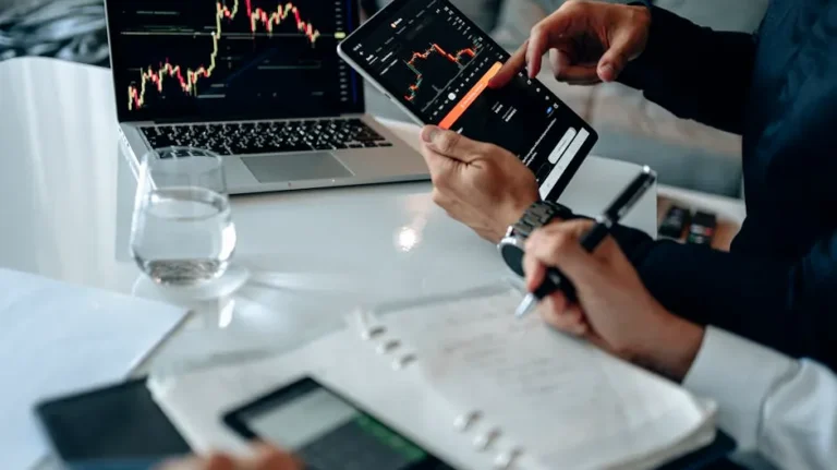 Business professionals reviewing financial charts on digital devices in a modern office setting.