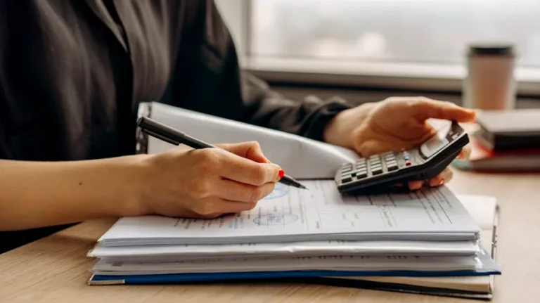 Close-up of person using a calculator with financial documents in an office.