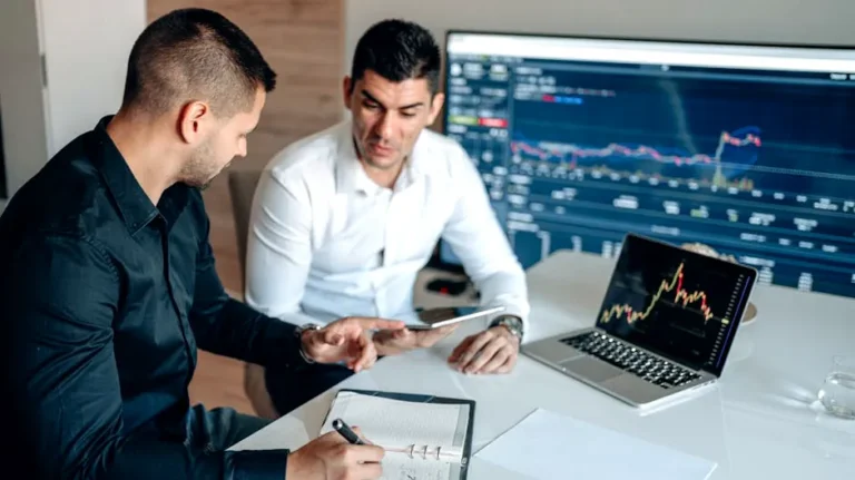 Two businessmen analyzing financial data on digital screens during a collaborative meeting.