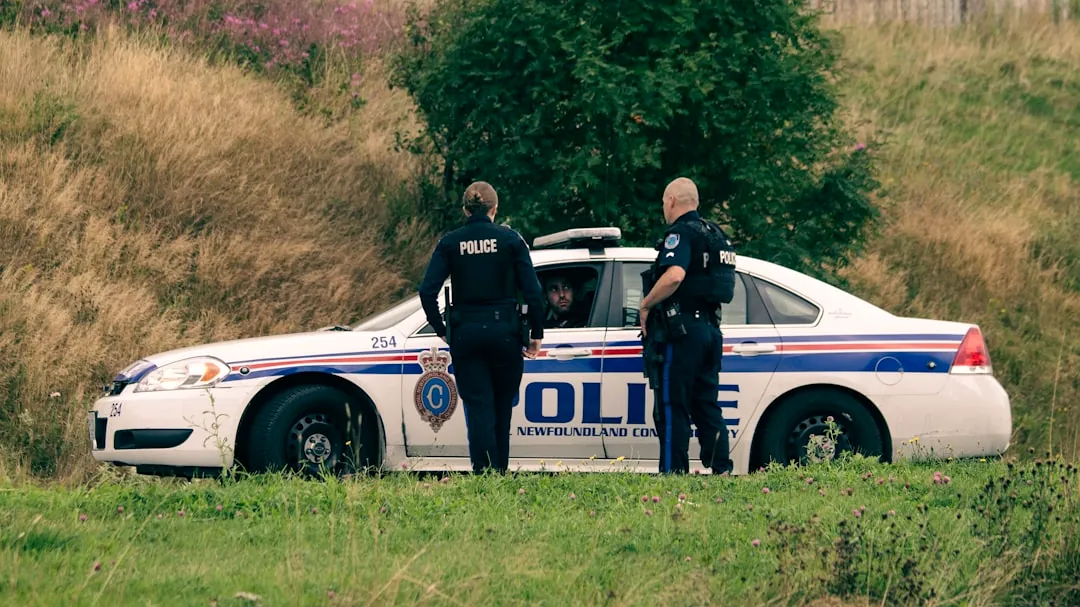 2 men standing beside white and blue police car